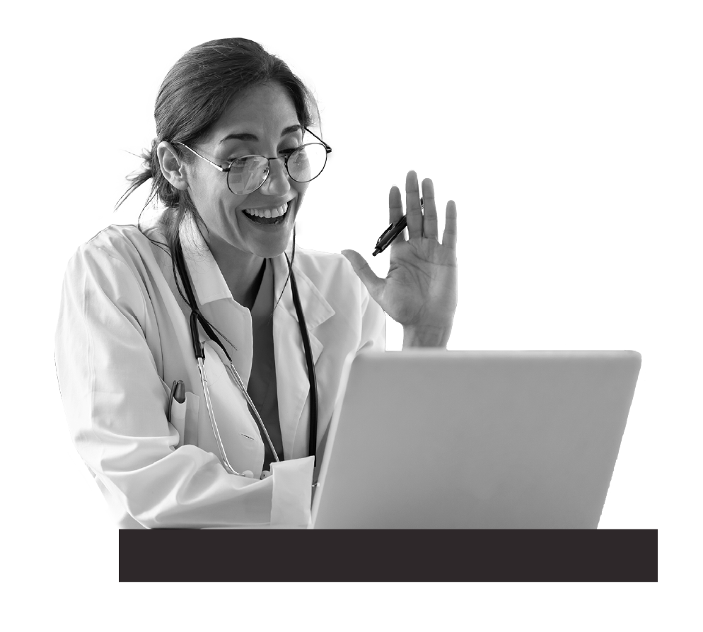 Woman in white coat with stethoscope around neck sitting in front of laptop smiling and waving.